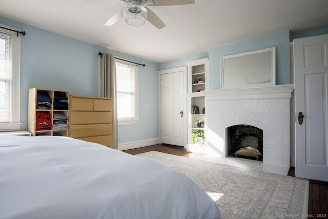 bedroom with a brick fireplace, a ceiling fan, baseboards, and wood finished floors