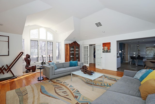 living room featuring baseboards, visible vents, hardwood / wood-style flooring, french doors, and high vaulted ceiling