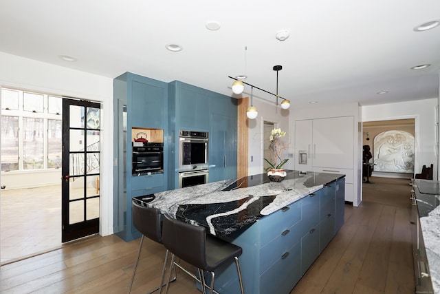 kitchen with double oven, dark wood-type flooring, light stone countertops, and blue cabinets