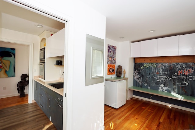 kitchen featuring light countertops, white cabinets, wood finished floors, built in microwave, and oven