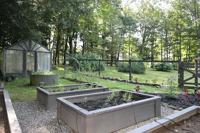 view of yard with a greenhouse, an outdoor structure, a vegetable garden, and fence