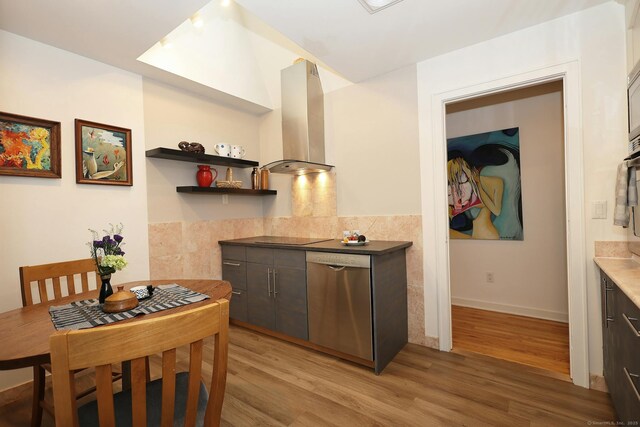 kitchen with open shelves, dark countertops, light wood-style floors, dishwasher, and wall chimney exhaust hood