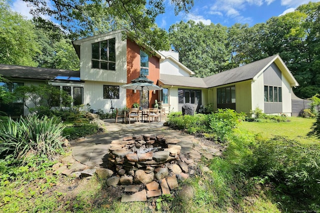 back of property featuring a patio area, an outdoor fire pit, a chimney, and a yard