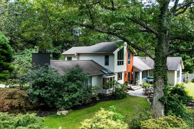 view of front of house with a front yard, roof with shingles, a patio, and a chimney