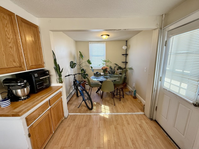 dining space with a baseboard heating unit, baseboards, light wood-style flooring, and a textured ceiling