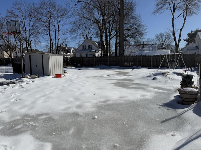 yard covered in snow with a storage shed, a fenced backyard, a playground, and an outdoor structure