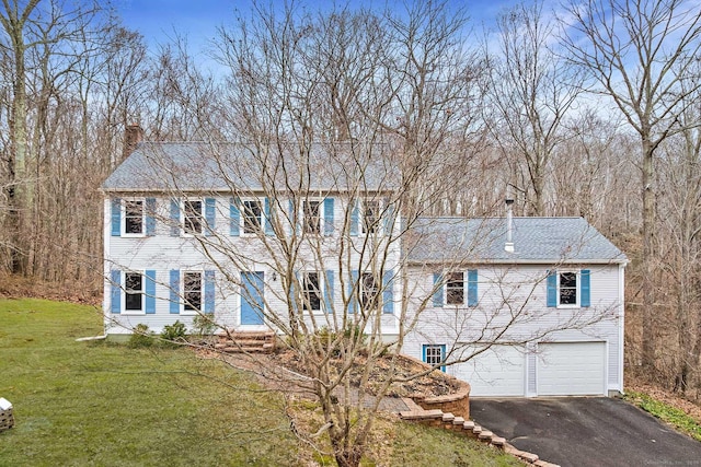 colonial home with a front yard, driveway, a chimney, and an attached garage