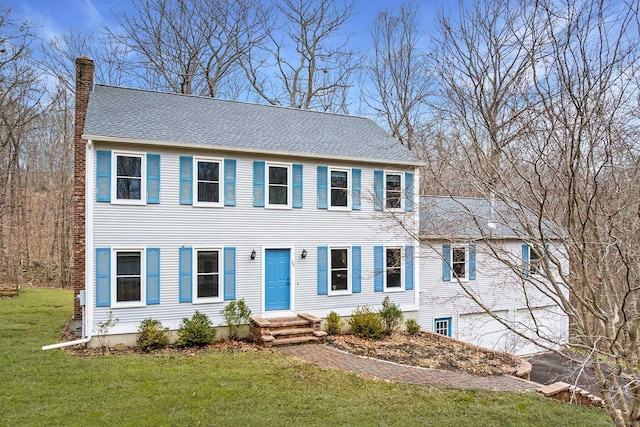 colonial house with a garage, driveway, roof with shingles, a chimney, and a front yard