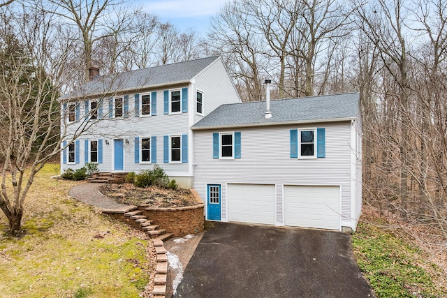 colonial inspired home featuring a garage, aphalt driveway, a chimney, and a shingled roof