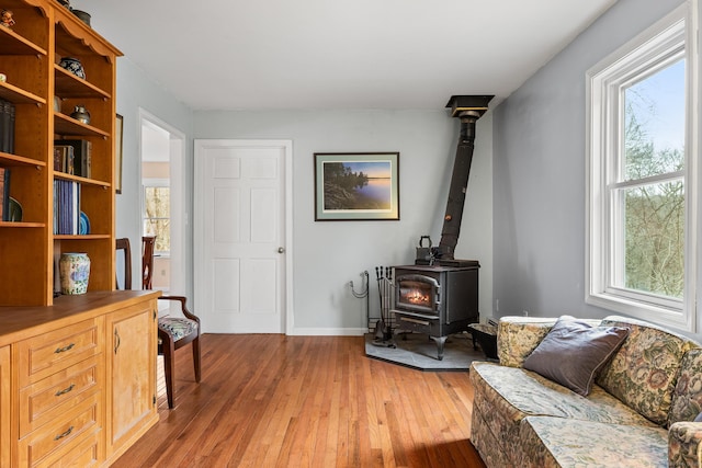 sitting room featuring a wood stove, light wood-style flooring, and baseboards