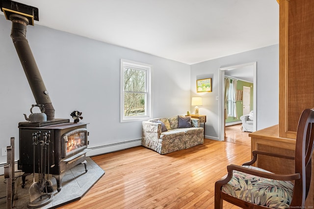 living area featuring baseboards, hardwood / wood-style flooring, a baseboard radiator, a wood stove, and baseboard heating