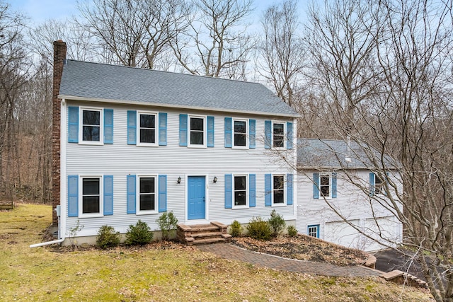 colonial inspired home with driveway, a garage, a shingled roof, a chimney, and a front lawn