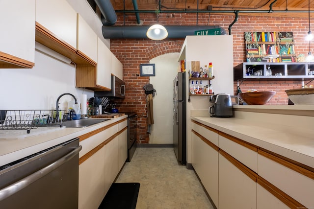 kitchen with appliances with stainless steel finishes, brick wall, light countertops, and a sink