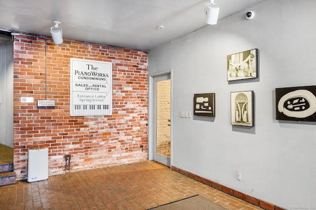 interior space featuring baseboards, brick floor, and brick wall