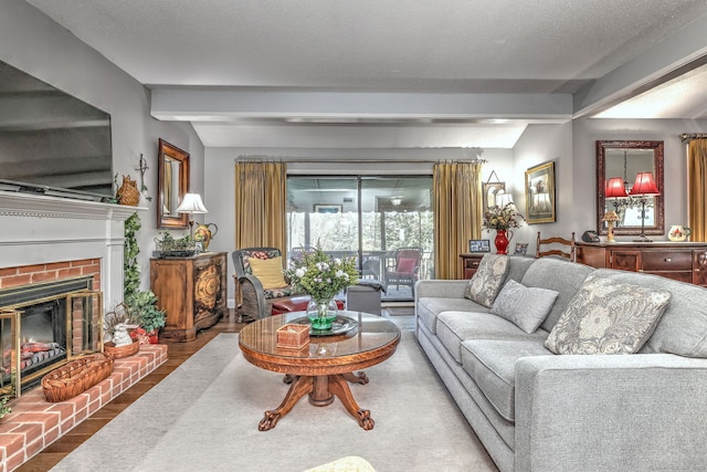 living area with a textured ceiling, a fireplace, beam ceiling, and wood finished floors