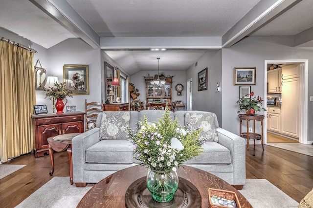 living room with a chandelier, vaulted ceiling, a textured ceiling, and hardwood / wood-style floors