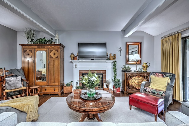 living area featuring beamed ceiling, a brick fireplace, and wood finished floors