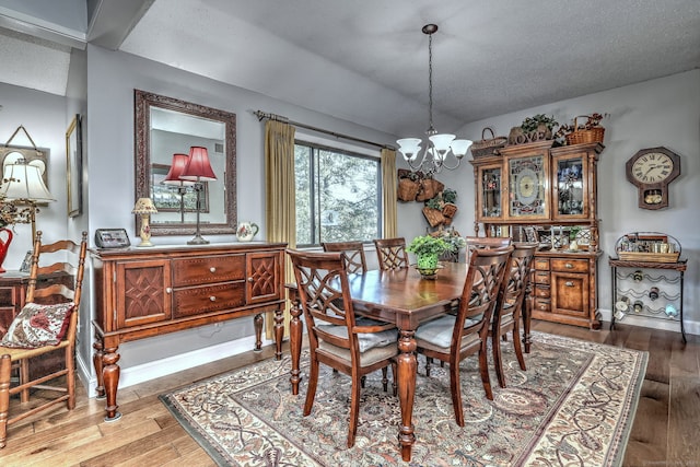 dining room with a notable chandelier, a textured ceiling, baseboards, and wood finished floors