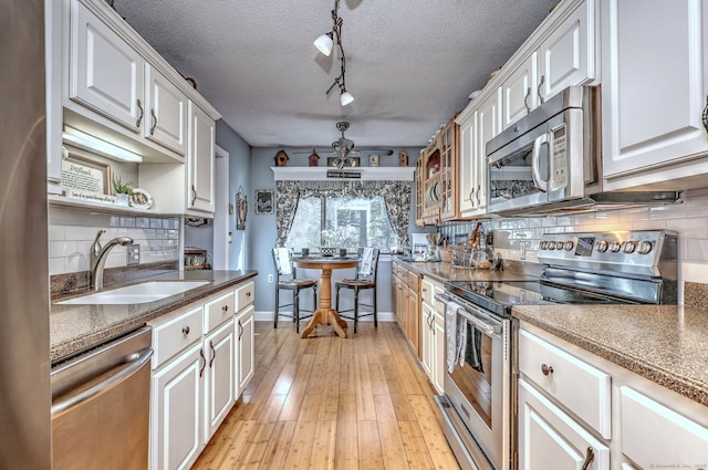 kitchen with open shelves, appliances with stainless steel finishes, light wood-style floors, white cabinets, and a sink