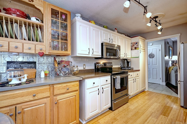 kitchen with a textured ceiling, stainless steel appliances, light wood-style floors, decorative backsplash, and glass insert cabinets