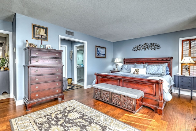 bedroom with baseboards, visible vents, connected bathroom, wood finished floors, and a textured ceiling