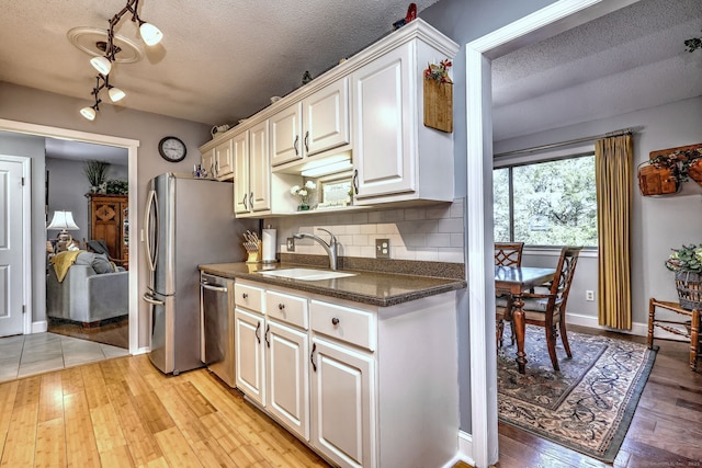 kitchen featuring dark countertops, light wood-style flooring, backsplash, a sink, and stainless steel dishwasher