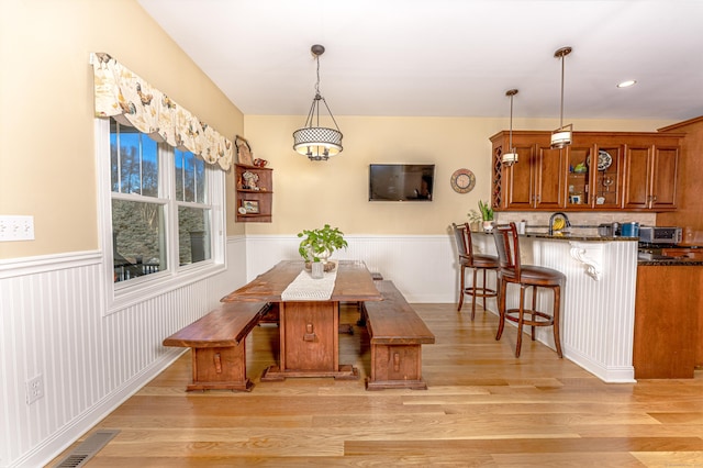 dining area with light wood-type flooring, breakfast area, wainscoting, and visible vents