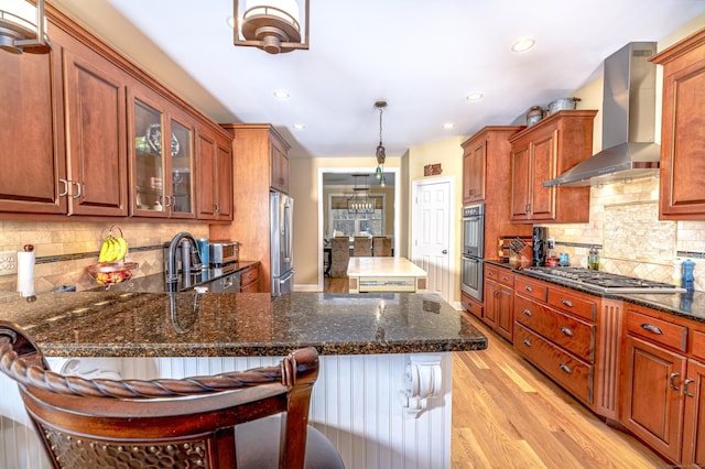 kitchen featuring light wood-style flooring, appliances with stainless steel finishes, glass insert cabinets, a sink, and wall chimney range hood