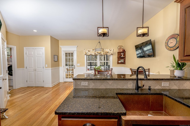 kitchen featuring hanging light fixtures, wainscoting, dark stone countertops, light wood-type flooring, and a peninsula