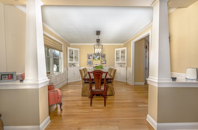 dining area with light wood-style floors, decorative columns, ornamental molding, and a notable chandelier