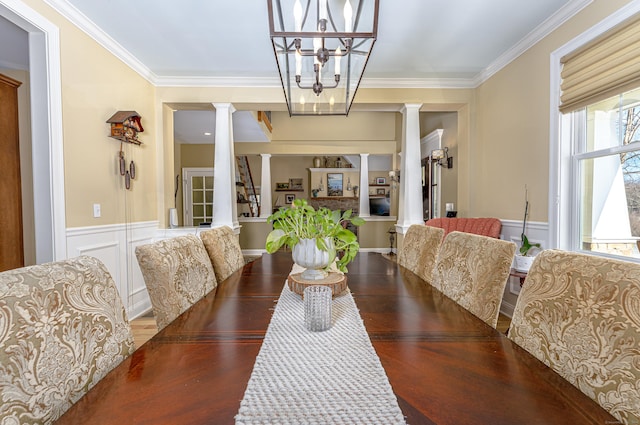 dining area featuring a wainscoted wall, decorative columns, ornamental molding, wood finished floors, and a chandelier