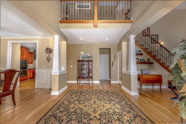 foyer featuring light wood-style flooring, stairway, and decorative columns