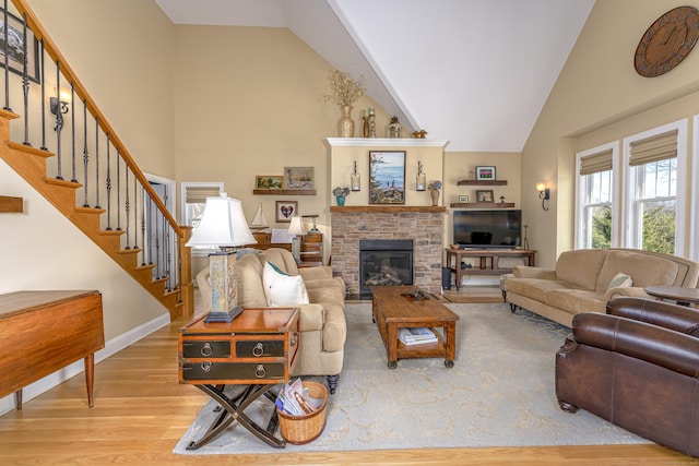 living area with high vaulted ceiling, wood finished floors, baseboards, stairs, and a glass covered fireplace