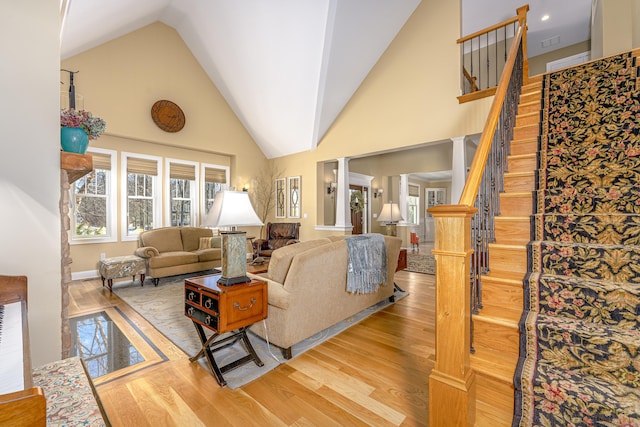 living room with light wood-style floors, high vaulted ceiling, ornate columns, and stairs