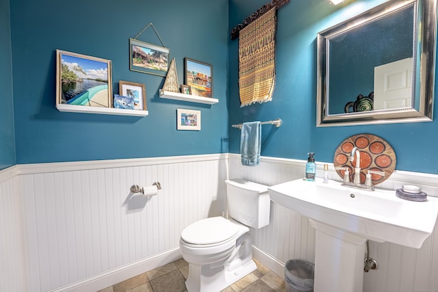 half bathroom featuring tile patterned flooring, a wainscoted wall, and toilet