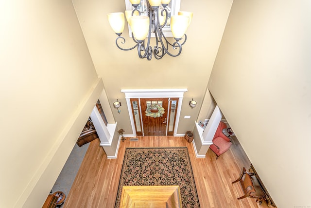 foyer entrance featuring baseboards, visible vents, wood finished floors, a high ceiling, and a notable chandelier