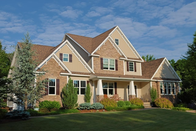 craftsman-style home featuring a front yard, covered porch, brick siding, and roof with shingles