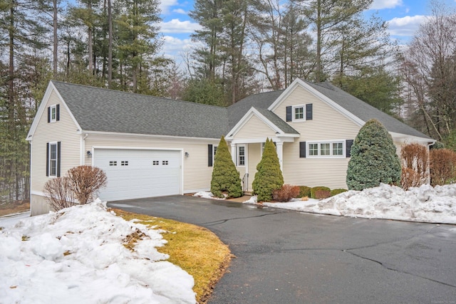 traditional home featuring an attached garage, a shingled roof, and aphalt driveway