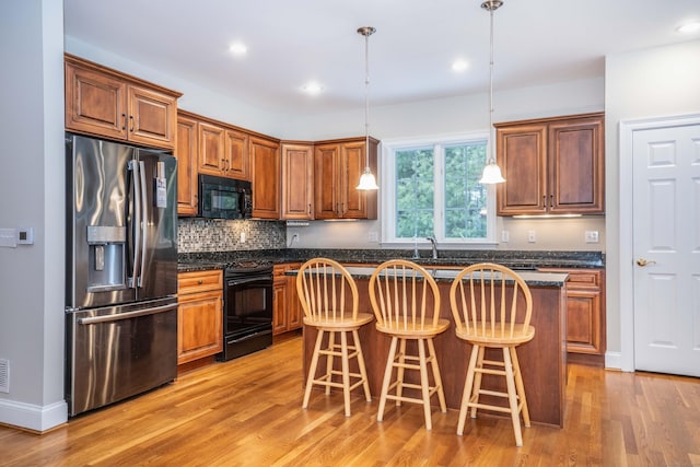 kitchen with a breakfast bar area, tasteful backsplash, light wood-style flooring, a kitchen island, and black appliances