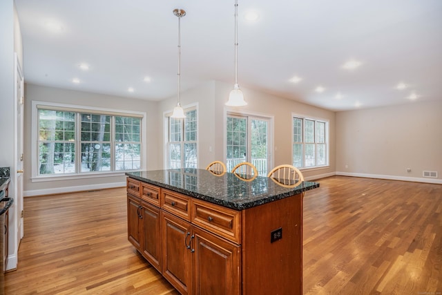 kitchen with light wood finished floors, baseboards, visible vents, a kitchen island, and brown cabinets