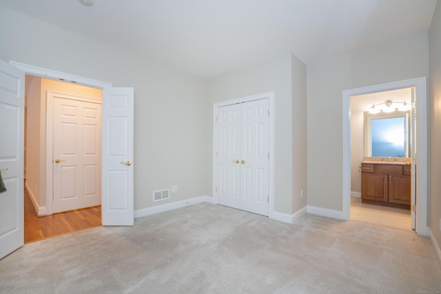 unfurnished bedroom featuring a closet, visible vents, light carpet, a sink, and baseboards