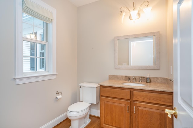 half bath with a healthy amount of sunlight, baseboards, toilet, and vanity