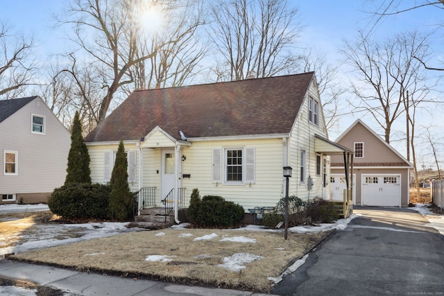 cape cod home featuring a garage, roof with shingles, and driveway