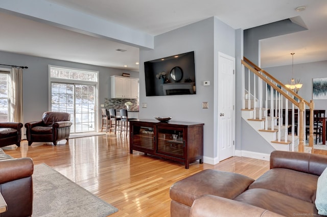 living room featuring baseboards, light wood-style flooring, stairway, and a notable chandelier