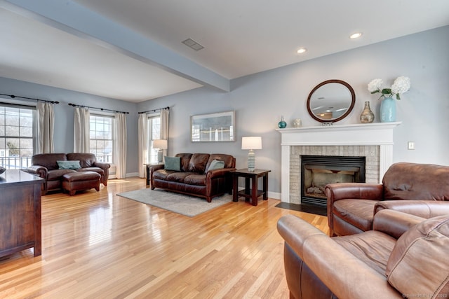 living room featuring a fireplace, visible vents, baseboards, light wood-style floors, and beam ceiling