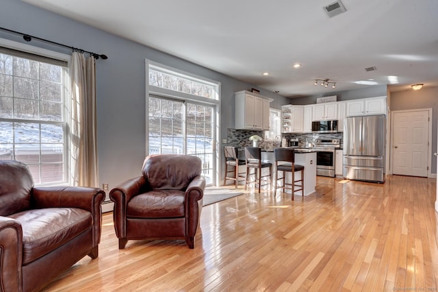 living area featuring light wood finished floors, visible vents, and baseboard heating