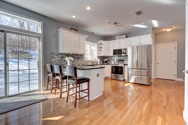 kitchen with tasteful backsplash, dark countertops, appliances with stainless steel finishes, a peninsula, and white cabinetry