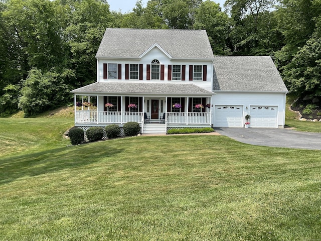 colonial house with aphalt driveway, a porch, an attached garage, roof with shingles, and a front lawn