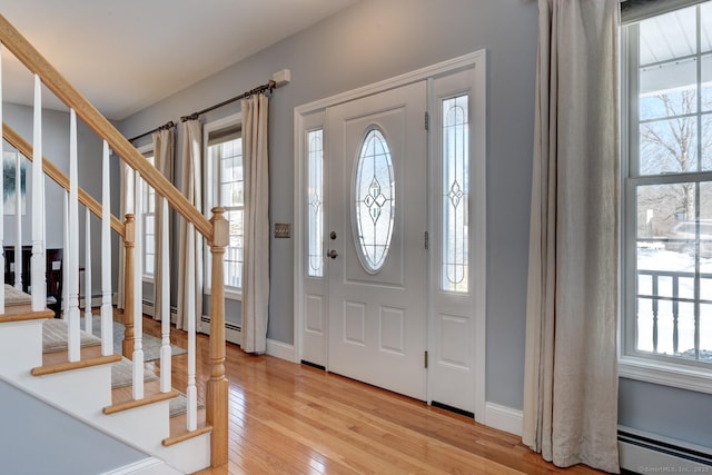 foyer entrance with stairs, baseboard heating, plenty of natural light, and light wood-style flooring