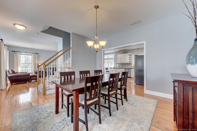 dining room with visible vents, stairway, light wood finished floors, and an inviting chandelier